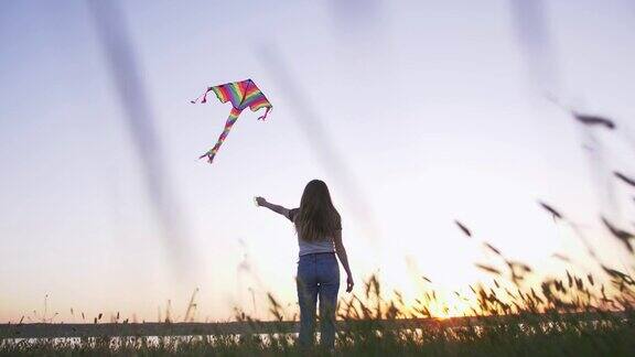 快乐的年轻女子玩风筝在一个林间空地与湖泊背景在夏季日落低角度的观点