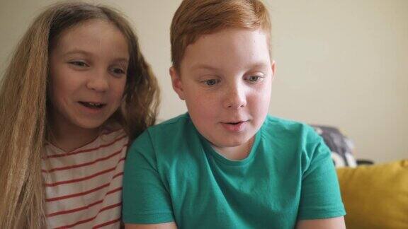 快乐的小男孩和女孩坐在房间的沙发上用智能手机看一段有趣的视频小弟弟和小妹妹在家里玩手机游戏孩子们花时间在一起