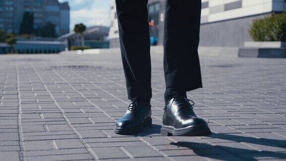 前视图脚的商人通勤工作一个自信的男人穿着皮鞋和西装走在商业区的街道上