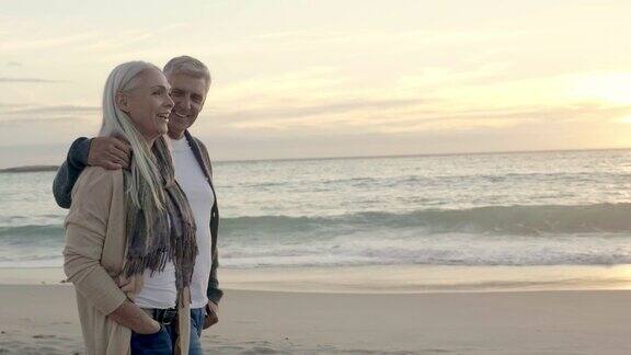 一对成熟的幸福夫妇在日落时分漫步在海滩上