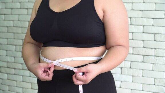 正面视图:身体泰国超重妇女测量她的肚子与卷尺