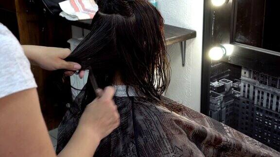女孩在理发店剪头发她坐在镜子前女发型师用剪刀剪她的发梢关闭了4k