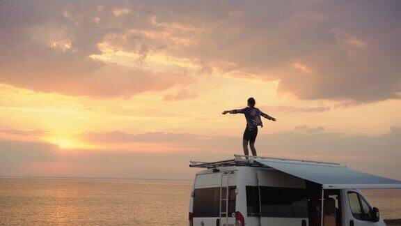 日落时分一个女人在海边露营车的屋顶上跳舞