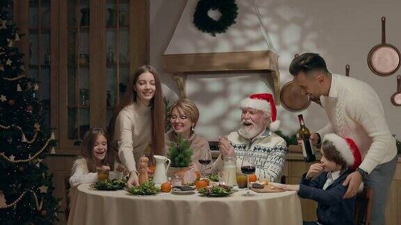家庭年夜饭餐桌上一个戴圣诞帽的老人和一个戴眼镜的女人两个孩子一个男孩一个女孩两个年轻人