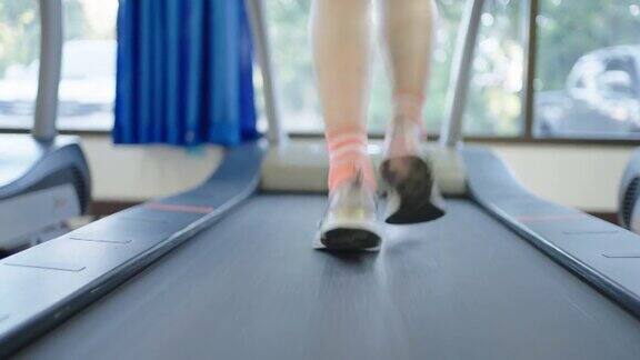 一位中年亚洲妇女在健身房的跑步机上慢跑