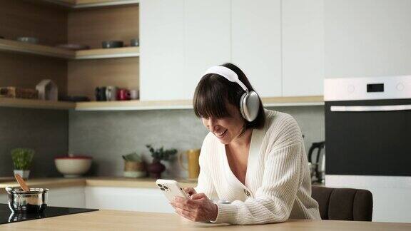 戴耳机的女人浏览手机在厨房里笑