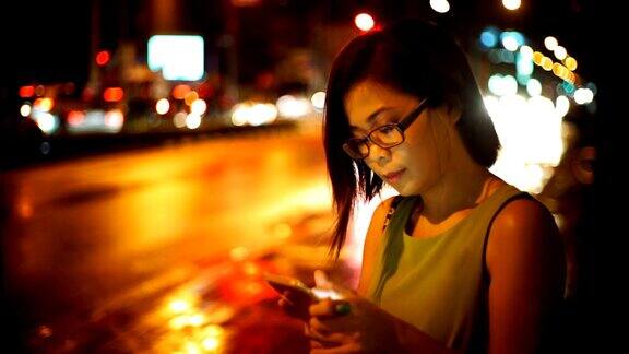 手机使用亚洲女性晚上在城市里使用智能手机