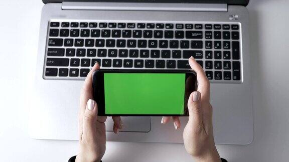 女性手握智能手机绿色屏幕色键概念笔记本电脑在背景最高镜头60帧秒
