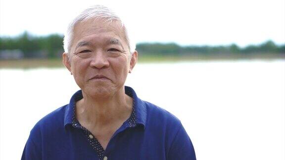快乐亚洲老人在以湖为背景的公园里快乐微笑的视频