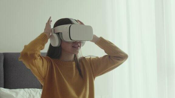 亚洲女性使用虚拟现实耳机或VR眼镜在家里的卧室