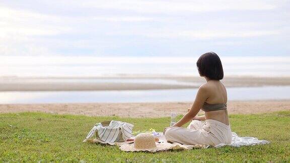 快乐的年轻女人坐在海边与野餐的东西一起冷却