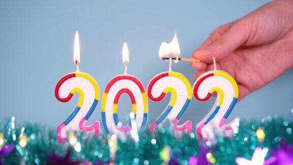 假日背景的手点燃彩色蜡烛2022与蓝色和丁香金丝2022年新年快乐概念4k分辨率的视频燃烧的2022蜡烛孤立在蓝色背景