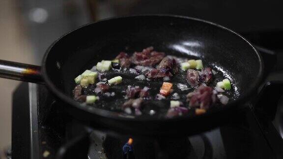 在厨房的煎锅里煎肉和蔬菜