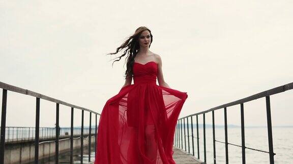 快乐的女人穿着漂亮的红色长裙走过码头