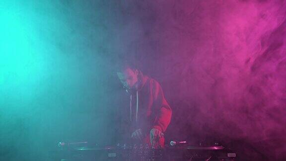 年轻酷炫的俱乐部DJ在烟雾弥漫的舞台上播放音乐夜总会唱片师在派对上用混音器和黑胶唱机混音
