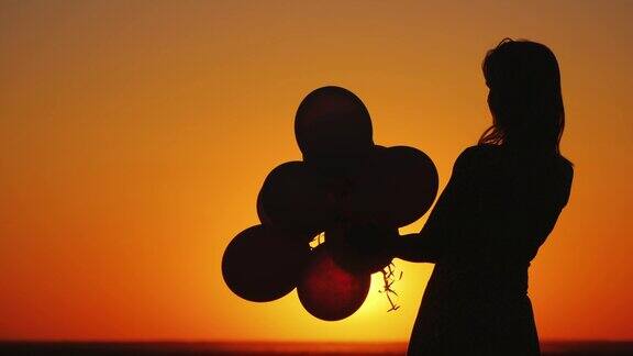一个年轻女子的剪影与气球在日落