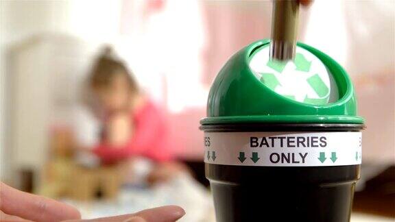女性将用过的电池放入家里专门的回收箱孩子在背景上玩耍电池只