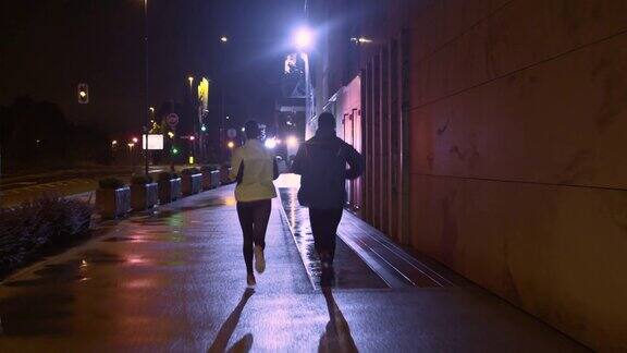 一对情侣在一个雨夜的城市街道上慢跑