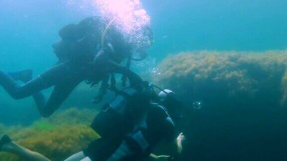 一名男性游客带着相机在水下潜水教练扶着他在水下