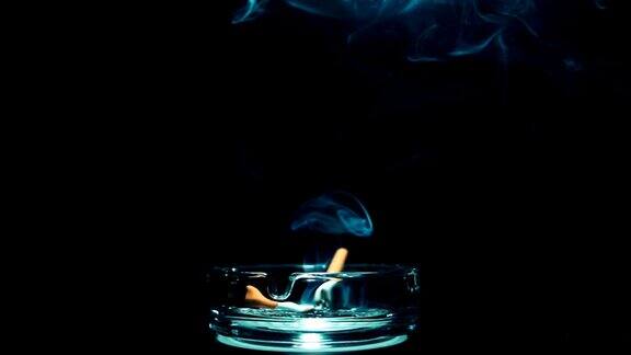 一只香烟躺在烟灰缸里冒烟旁边是一只已经抽过的香烟