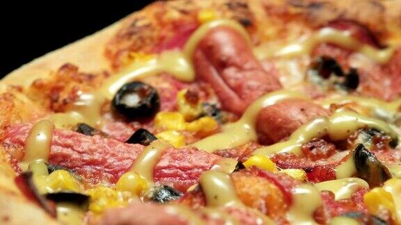 特写镜头:旋转的热披萨配香肠、橄榄、奶酪和芥末加蜂蜜