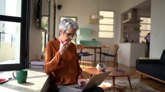 高级女性在家工作使用笔记本电脑用智能手机发送音频信息