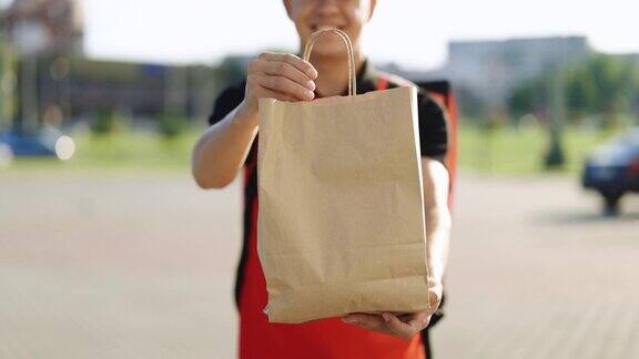 开心的快递员拿着装着食物的包裹看着镜头微笑着正青年信使特写肖像送货上门服务