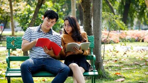 两个亚洲年轻的大学生或情侣正在户外公园的长椅上看书