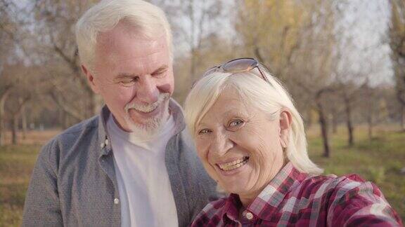 微笑的白人退休夫妇在镜头前挥手的特写成熟的欧洲家庭站在阳光下的秋天森林白头偕老永恒的爱情观