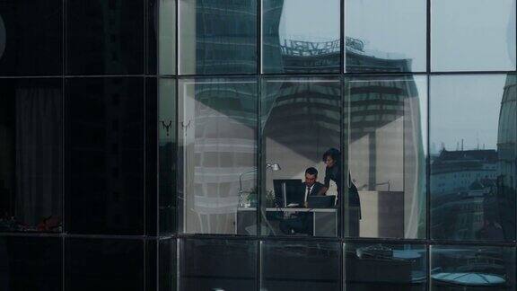 从摩天大楼外的航拍镜头:商人和女商人坐在办公室窗户的办公桌前谈生意在大城市工作的金融区和商人的飞行镜头