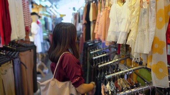 年轻美丽的亚洲女人选择和试衣服在购物中心市场街