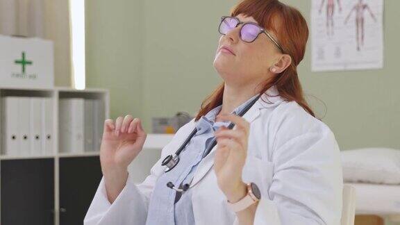 一段4k视频显示一名女医生坐在办公桌前做伸展运动