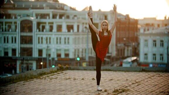 年轻的女芭蕾舞演员在屋顶上训练-站在展示她伸展的姿势-日落
