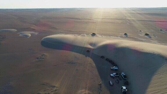 4K空中缩放的游客和他们的4x4车辆露营在新月形状的沙丘中心纳米比亚沙漠纳米比亚