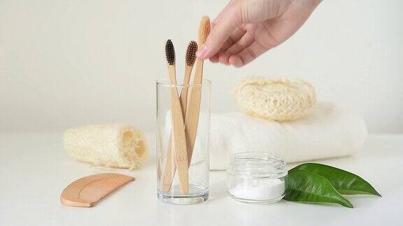 女人在浴室用手从玻璃里拿出竹制的木质牙刷零浪费和卫生理念