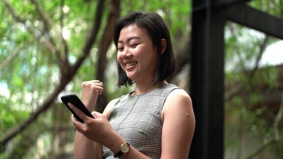 激动的亚洲女商人在智能手机上收到了好消息