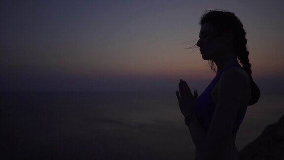 平静和女孩练习瑜伽和冥想日落在海边在悬崖上女运动员在祈祷时手拉手精神性正念和健康生活方式