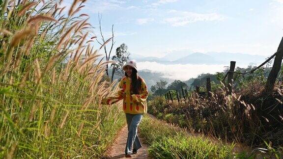 年轻的亚洲妇女穿着毛衣走在草原和山景在农村在早上
