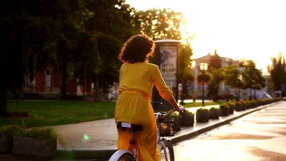 一个不认识的女人骑着一辆城市自行车与篮子和鲜花在城市中心在黎明享受她的时间清晨镜头光晕慢动作拍摄