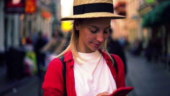 年轻女子戴着时髦的帽子在城市街道上摸着头发拿着手机的慢动作效果