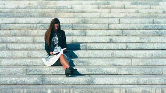 一个年轻的白人少女拿着一本书坐在大学楼梯上的肖像