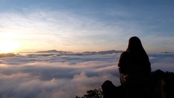 一个女旅人坐在山顶上看日出和雾海