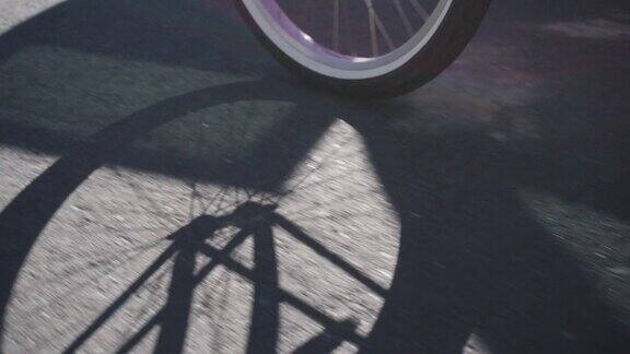 一辆自行车的轮子和辐条投射在人行道上的影子而一个女人穿着皮靴踏板在一个阳光明媚的日子