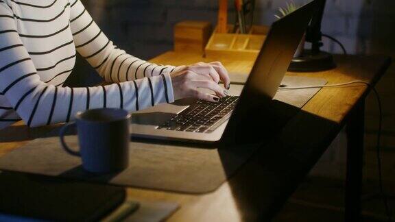 一个女人坐在办公室的桌子前在笔记本电脑上打字特写没有脸