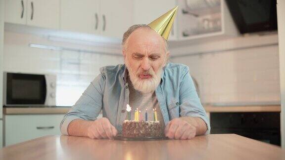 孤独的白发老人戴着派对帽吹灭生日蛋糕上的蜡烛