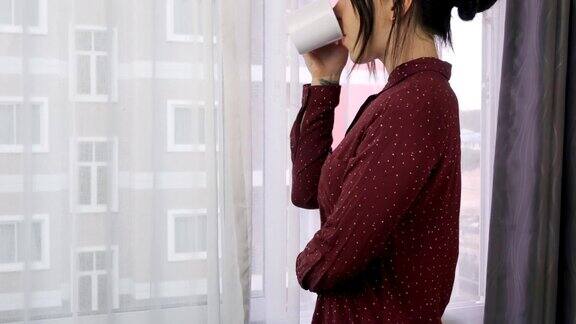 一位年轻女子正站在窗边喝咖啡