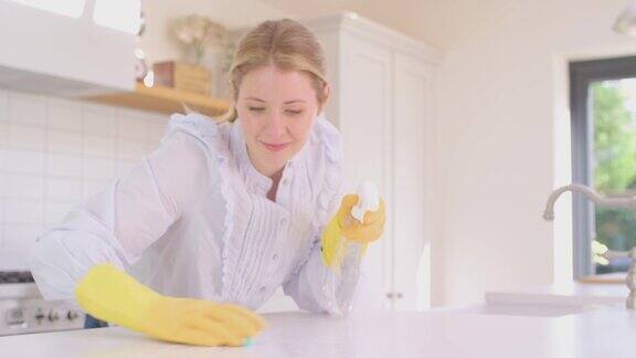 在家做家务的女人戴着橡胶手套用喷雾和布清洁厨房柜台