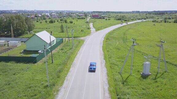 从无人机上看蓝色复古的俄罗斯汽车在村庄的道路上行驶