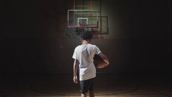 在黑暗的球场上行走的小篮球运动员