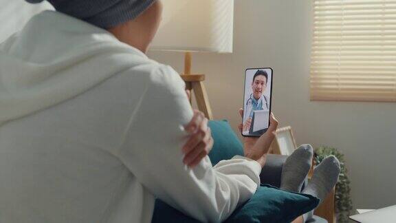 年轻的亚洲妇女生病的癌症使用电话交谈医生坐在沙发上的客厅在家里